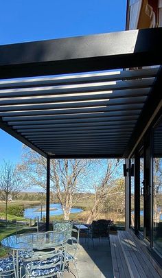 an outdoor patio with table and chairs under a pergolated roof over looking a body of water