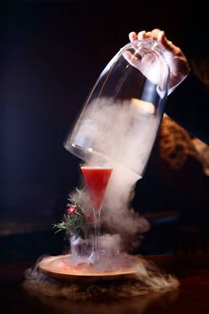 a person pouring liquid into a glass on top of a wooden plate with mist coming out of it