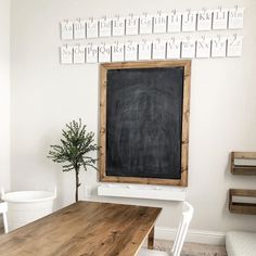 a chalkboard is hanging on the wall above a wooden table with white chairs and a potted plant