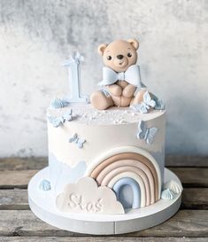 a teddy bear is sitting on top of a baby's first birthday cake with rainbows and clouds