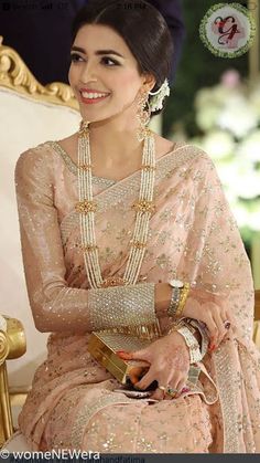 a woman in a pink sari sitting on a gold chair with pearls around her neck