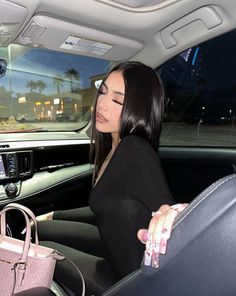 a woman sitting in the back seat of a car holding a pink purse and looking at her cell phone