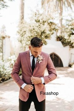 a man in a pink suit and black tie is looking down at his pocket square