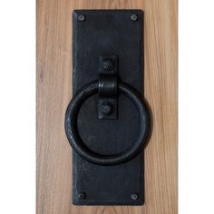 an old black door handle on a wooden surface with a metal ring at the center