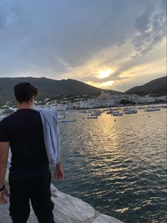 a man standing on the edge of a cliff looking out at boats in the water