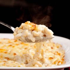 a spoon full of macaroni and cheese being lifted from a white plate