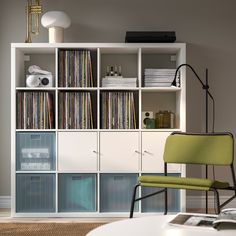 a white bookcase filled with lots of books next to a green chair and lamp