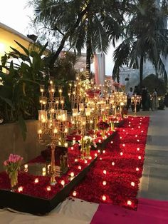 many candles are lit on the ground in front of red flowers and greenery at night