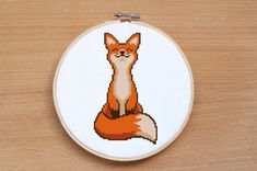 a cross stitch fox sitting on top of a wooden table