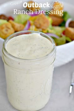 a bowl of salad with dressing next to it and a fork on the table in front