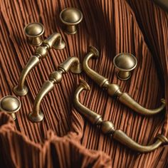 an assortment of antique brass handles and knobs on a brown pleated fabric background