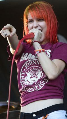 a woman with red hair and piercings on her chest holding a microphone in front of her mouth