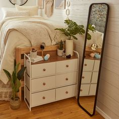 a bedroom with a bed, dresser and mirror in the corner next to a potted plant