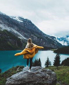 a woman standing on top of a rock next to a lake