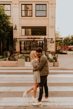 a man and woman standing in front of a tall building with their arms around each other