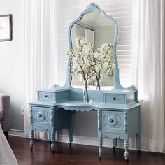 a blue dresser with a mirror and vase on it in front of a white window