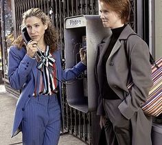 two women standing next to each other on the street talking on their cell phones,