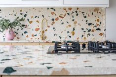 a kitchen with marble counter tops and white cupboards next to a pink vase filled with flowers