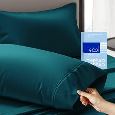 a person is holding up a blue sheet on top of a bed with green sheets