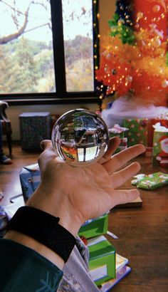 a hand holding a crystal ball in front of a christmas tree