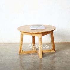 a round wooden table with a book on it's top sitting in front of a white wall