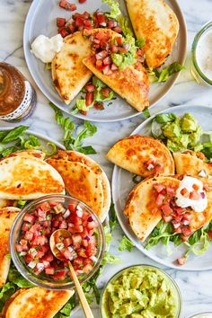 three plates filled with quesadillas and guacamole on a marble table