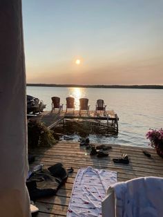 the sun is setting over the water and some chairs are set up on the dock