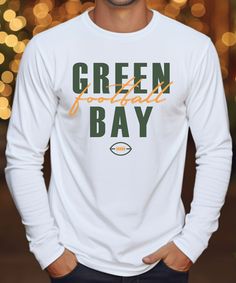 a man wearing a green bay long sleeve t - shirt in front of christmas lights