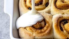 cinnamon rolls with icing being drizzled on top in a baking dish