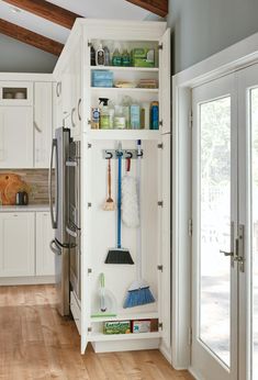 an organized kitchen with white cabinets and wood flooring, including brooms and cleaning supplies