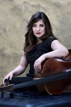 a woman sitting on top of a blue suitcase holding a violin and posing for the camera