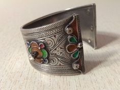 This is a Beautiful silver berber bracelet from the Anti Atlas region in Morocco. The decoration is very refined, there's some remains of black deco and enamel in yellow and green. This bracelet shows an exquisite quality of engraved work with flower motifs. The center stone is an glass in red color. Min Width : 2,5 cm (0,98 inches) Max Width : 4,2 cm (1,6 inches) Inner diameter : 5,8 cm (2,3 inches) Weight : 56,7 g Moroccan Jewelry, Flower Motifs, Yellow And Green, Photo Jewelry, Cross Pendant, Red Color, Morocco, 6 Inches, Antique Silver