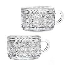 two glass mugs sitting next to each other on a white surface with an intricate design