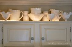 white glass vases and pitchers on top of a cabinet