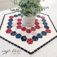 a potted plant sitting on top of a quilted placemat with red, white and blue hexagonal designs