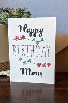 a card with the words happy birthday mom written in black and red on it, next to a potted plant