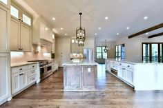 a large kitchen with white cabinets and an island in the middle of the room is lit by pendant lights