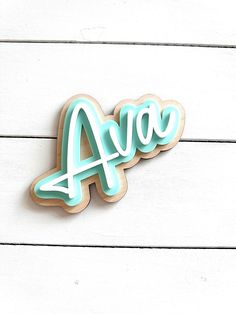 a cookie with the word ava spelled in blue icing on a white wooden surface