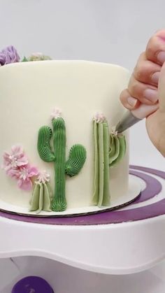 a person cutting into a cake decorated with cactus and flowers