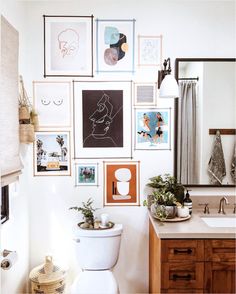 a white toilet sitting under a bathroom mirror next to a wooden cabinet with pictures on it