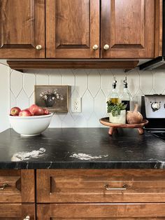 a bowl of fruit is sitting on the counter in this kitchen with dark wood cabinets and white tile backsplash