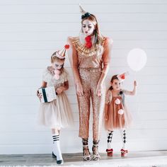 three girls dressed up as clowns standing in front of a white wall with balloons