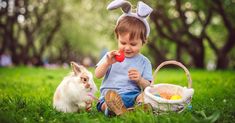 a little boy sitting in the grass with two small rabbits next to him and an easter basket