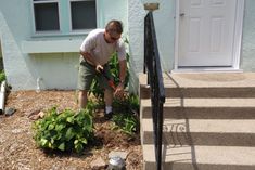 a man is digging in the dirt near some flowers and plants on the ground next to a house