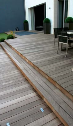 a wooden deck with chairs and table next to grass in front of it, on a patio