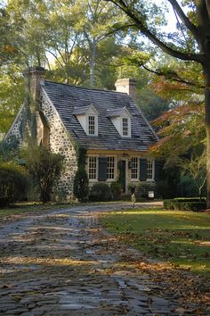 a cobblestone road leading to a stone house in the fall with leaves on the ground