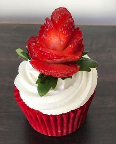 a red cupcake with white frosting and a strawberry on top is sitting on a table