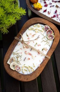 two trays filled with different types of flowers on top of a wooden table next to potted plants