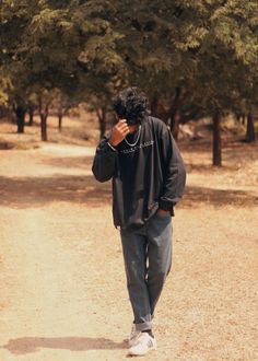 a man walking down a dirt road while talking on a cell phone with trees in the background