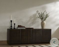 a vase with some plants on top of it next to a wooden sideboard in a room